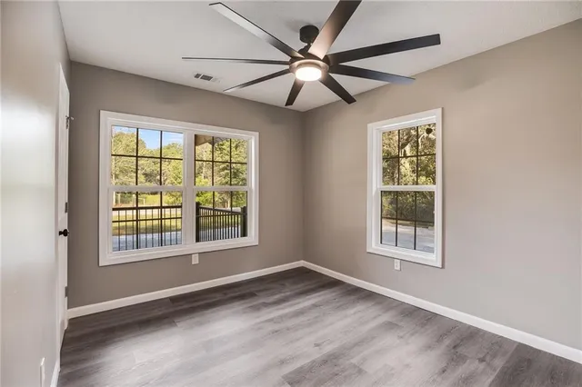 an empty room with wooden floor fan and windows