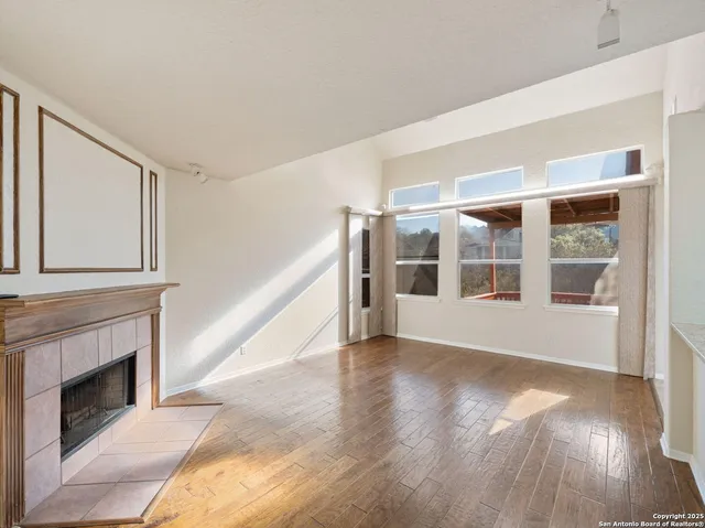 a view of an empty room with wooden floor fireplace and a window