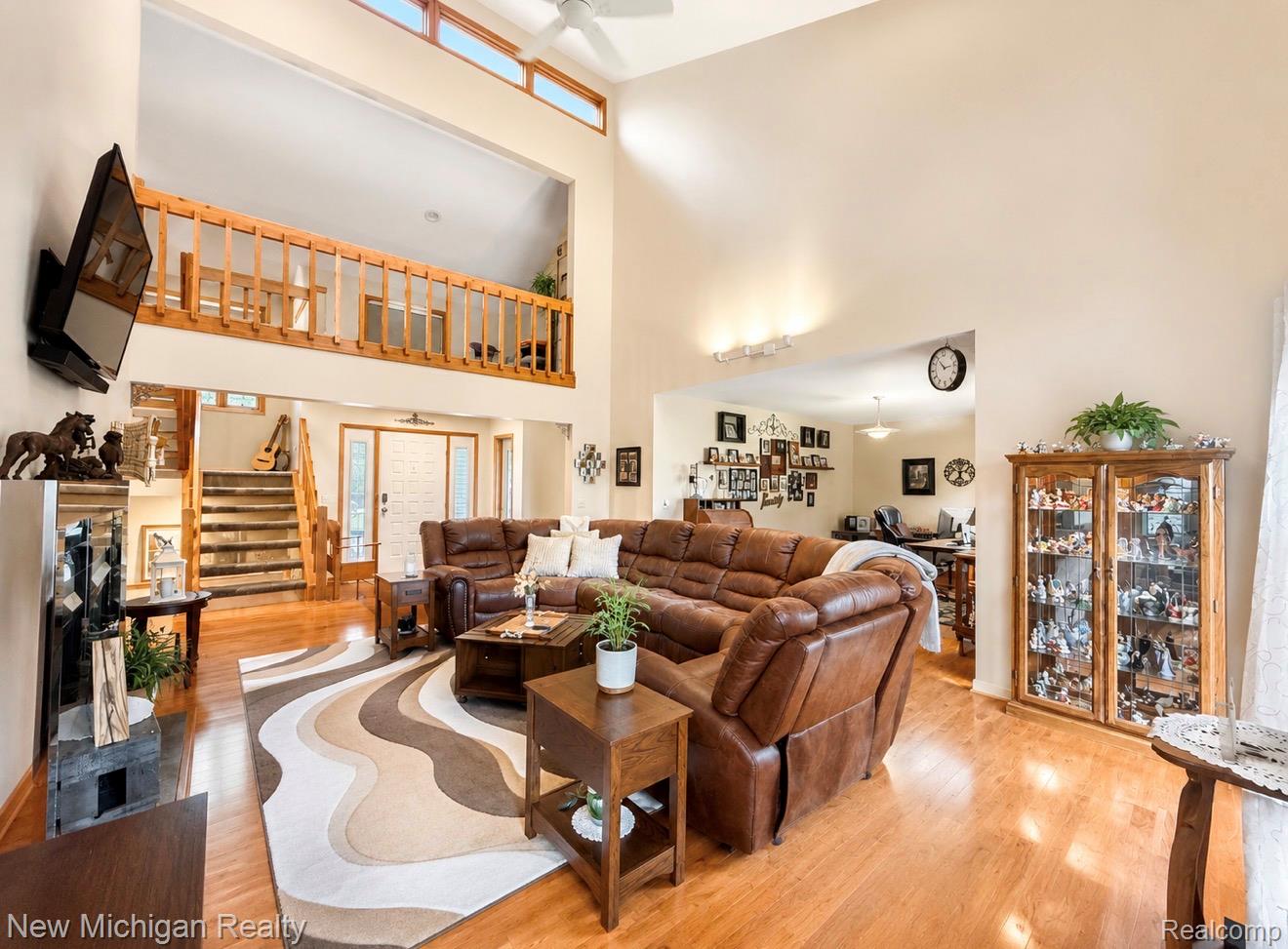 7156 East River Road Flushing, MI 48433 - Photo 14 of 35 Open-concept living space with wood-finish flooring, a two-story vaulted ceiling, an upper-level balcony with wood railing, clerestory windows, and a prominent wood staircase