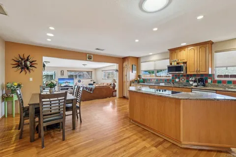 a kitchen with stainless steel appliances kitchen island granite countertop a refrigerator a stove top oven and a dining table with wooden floor