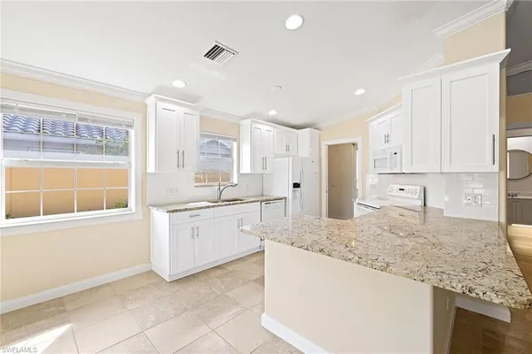 a large kitchen with granite countertop a sink and white cabinets
