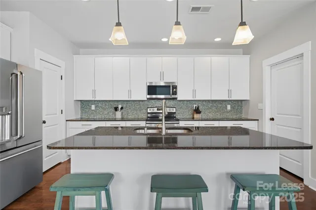 a kitchen with stainless steel appliances granite countertop a sink a stove a refrigerator cabinets and chairs