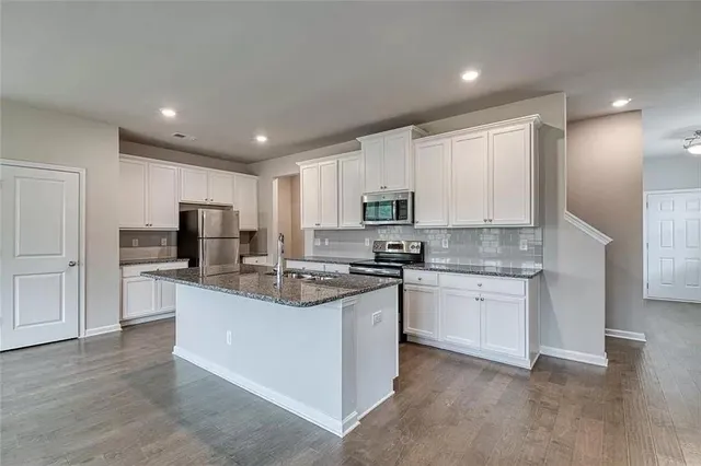 a kitchen with stainless steel appliances granite countertop a stove top oven a sink a refrigerator and white cabinets with wooden floor