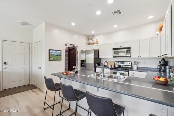 a kitchen with stainless steel appliances a sink a stove a refrigerator cabinets and chairs