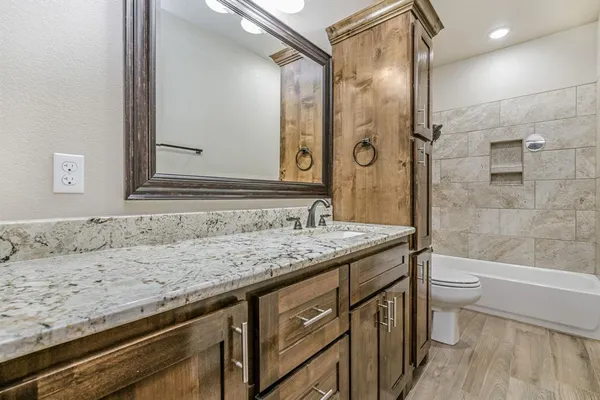 a bathroom with a granite countertop sink a toilet a mirror and shower