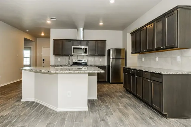 a kitchen with stainless steel appliances granite countertop a stove a sink dishwasher a refrigerator and a microwave oven on the wooden floor