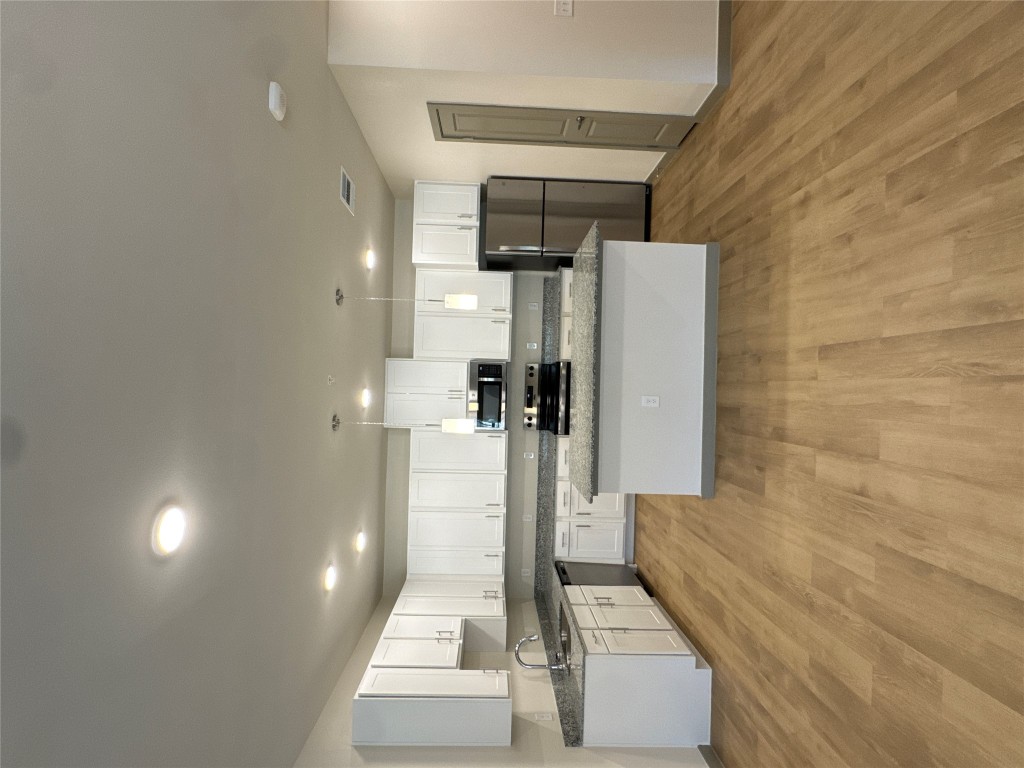 Kitchen featuring hanging light fixtures, white cabinetry, appliances with stainless steel finishes, a kitchen island, and light wood-style flooring