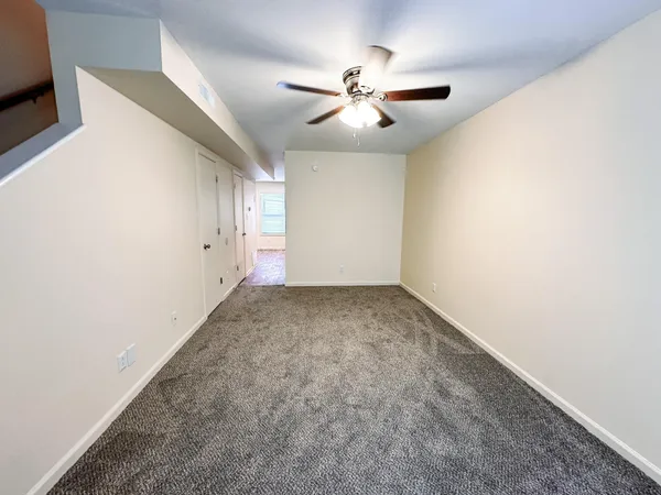 an empty room with a chandelier fan and windows