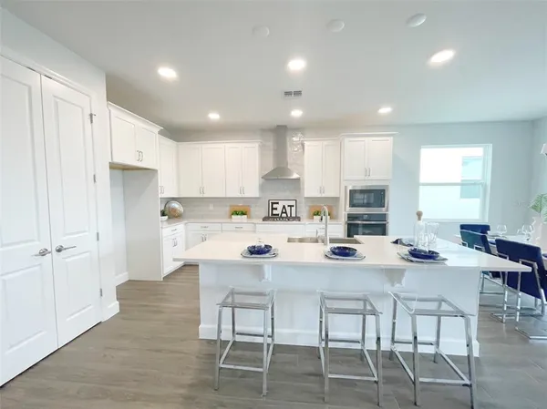 a kitchen with kitchen island granite countertop a dining table chairs refrigerator and cabinets