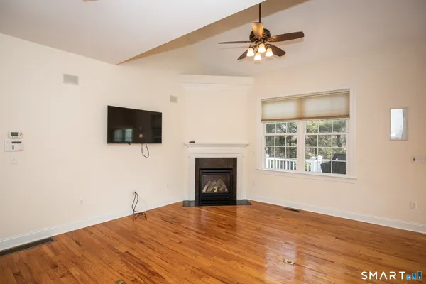 a view of an empty room with wooden floor fireplace and a window