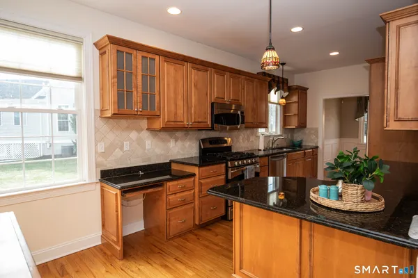 a kitchen with granite countertop stainless steel appliances a sink a stove and a wooden floor