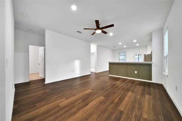 a view of an empty room with wooden floor and a ceiling fan