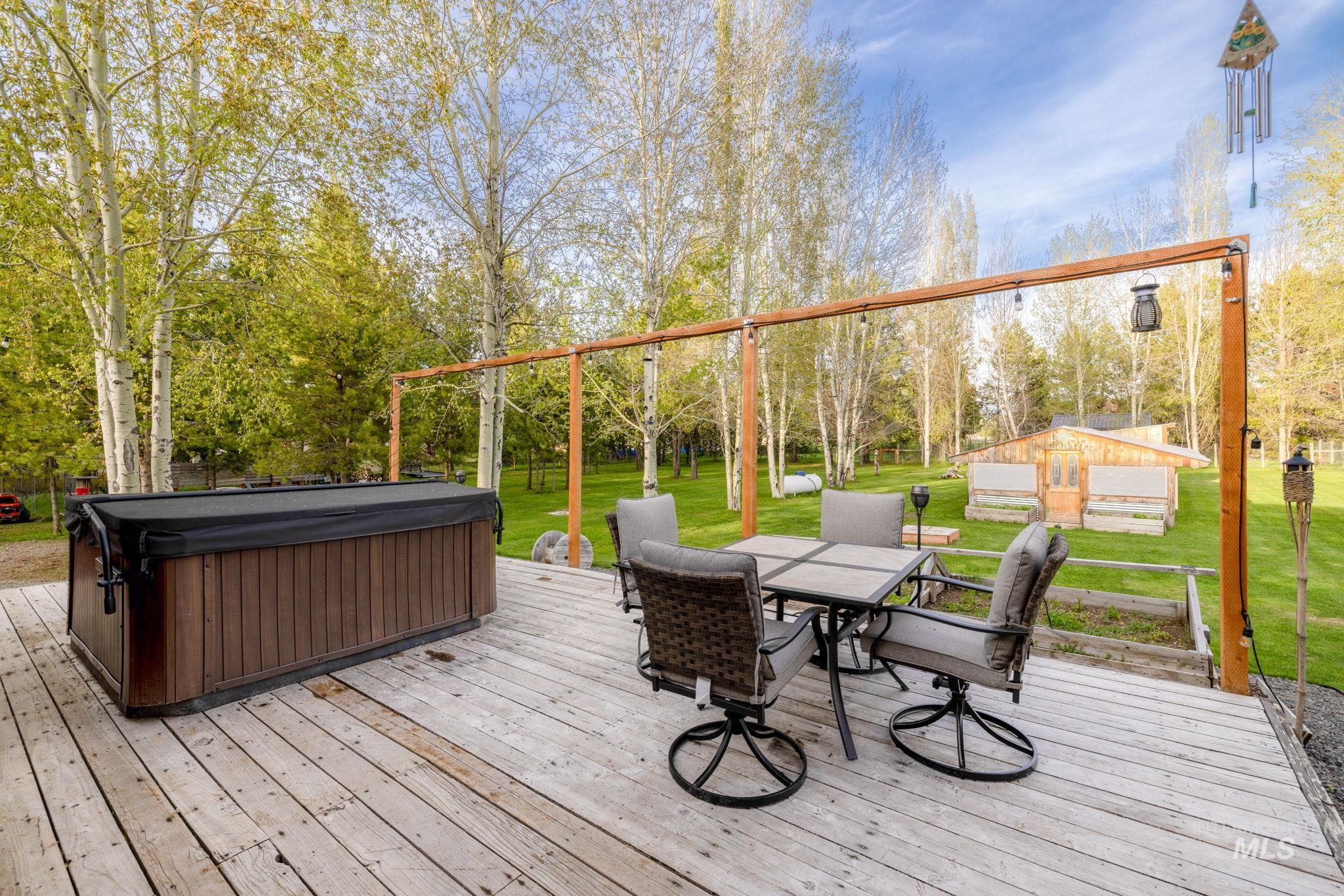12954 Upland Road Donnelly, ID 83615 - Photo 32 of 41 Wooden terrace with outdoor dining space, a lawn, a hot tub, and view of wooded area