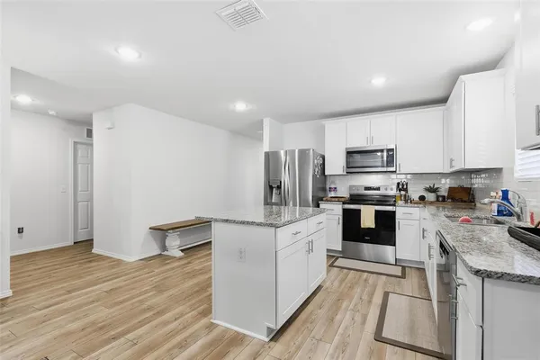 a kitchen with stainless steel appliances a stove a sink a refrigerator white cabinets and wooden floor