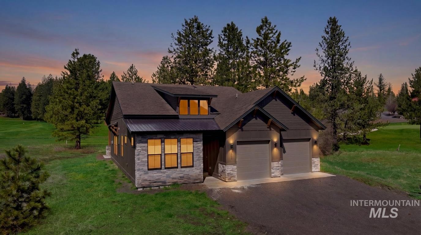 View of front facade with a lawn, stone siding, driveway, and an attached garage
