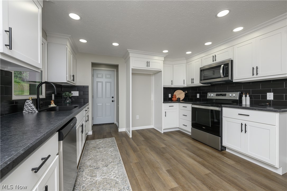 4855 4th Street Northwest Canton, OH 44708 - Photo 4 of 25 Kitchen with dark hardwood / wood-style flooring, white cabinets, sink, appliances with stainless steel finishes, and backsplash