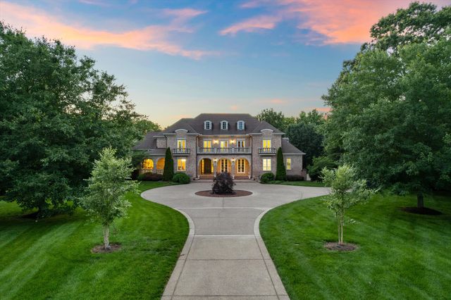 a view of a brick house with a big yard plants and large trees