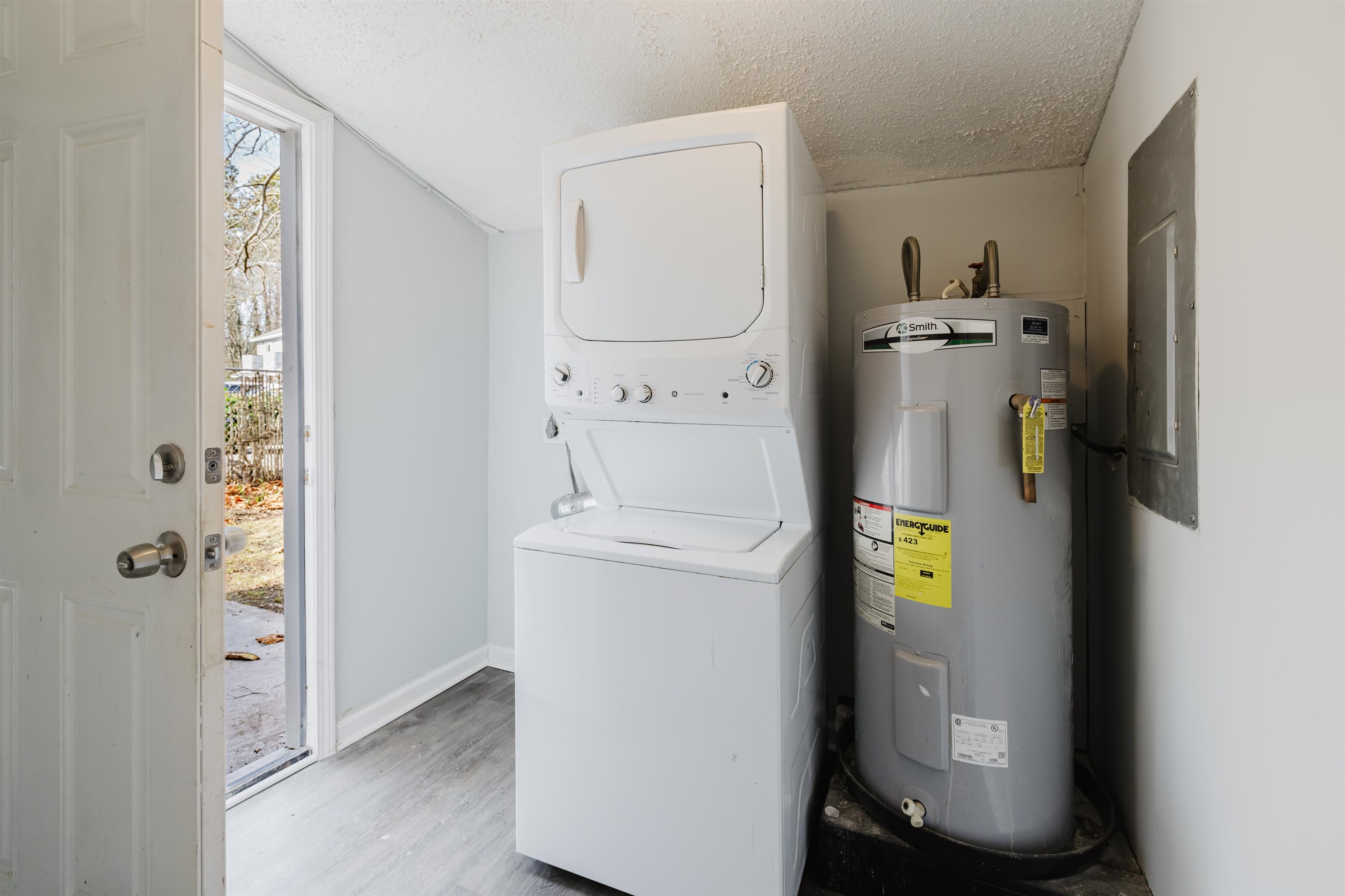 90 Freedom Way Myrtle Beach, SC 29577 - Photo 11 of 16 Washroom featuring electric water heater, a textured ceiling, electric panel, stacked washer and clothes dryer, and light wood-style flooring