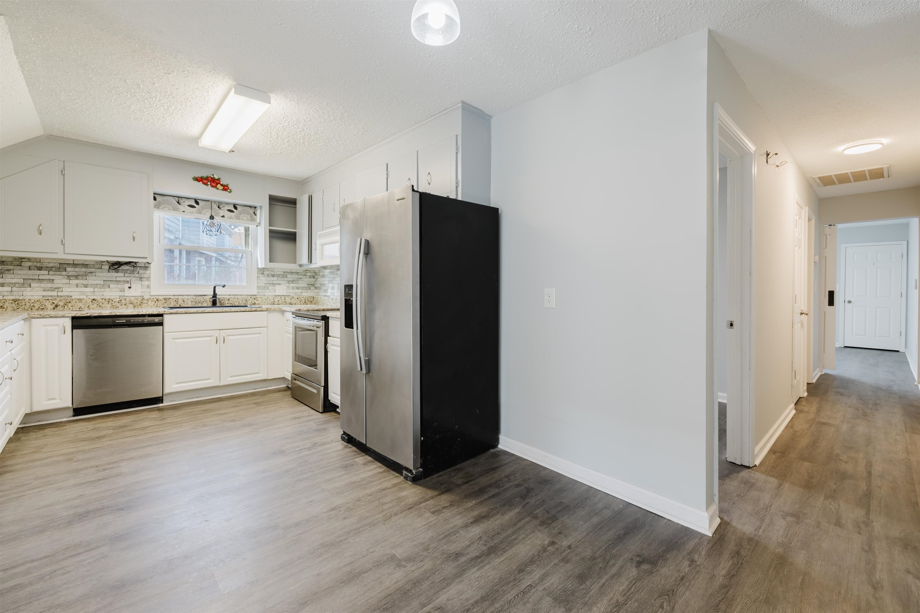 90 Freedom Way Myrtle Beach, SC 29577 - Photo 3 of 16 Kitchen with appliances with stainless steel finishes, white cabinetry, backsplash, a textured ceiling, and light wood-type flooring