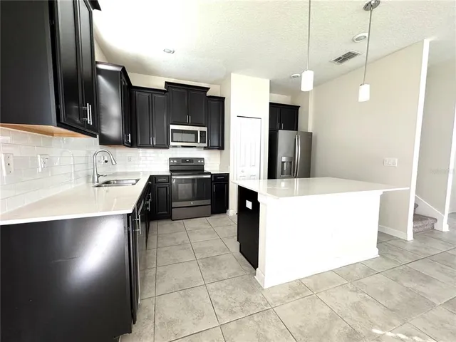 a large kitchen with kitchen island a sink a counter and stainless steel appliances