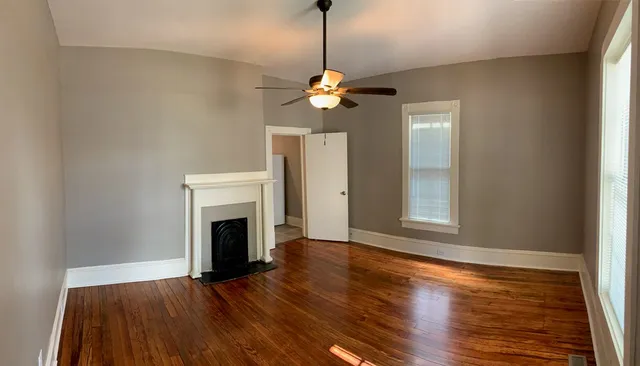 a view of a livingroom with a fireplace a ceiling fan and wooden floor