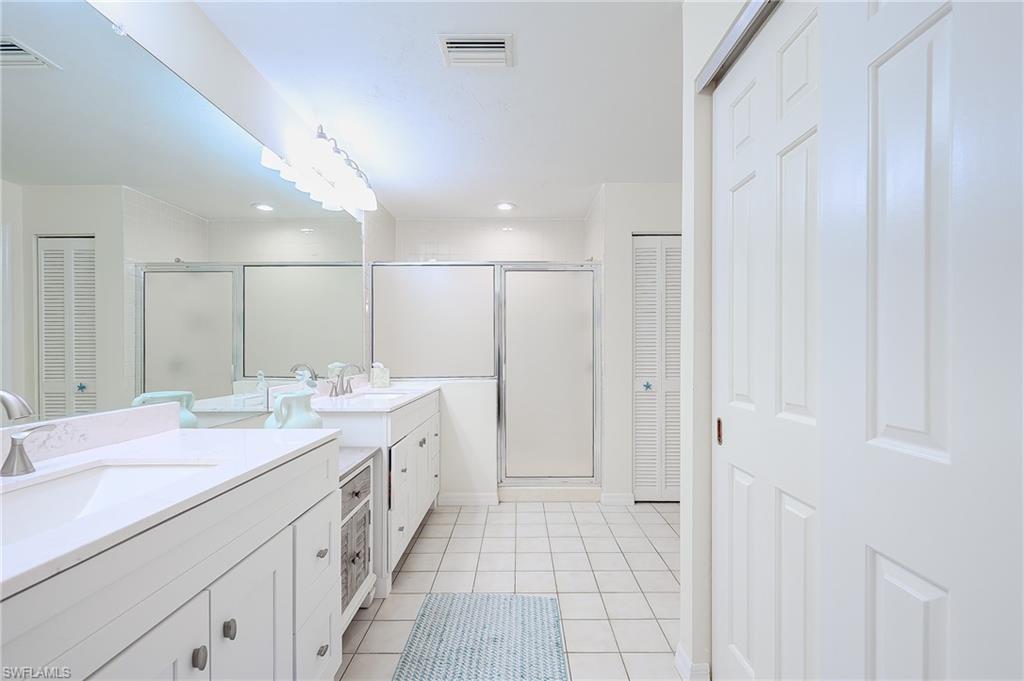 833 Reef Point Circle Naples, FL 34108 - Photo 21 of 41 Bathroom with a closet, two vanities, a stall shower, and light tile patterned floors