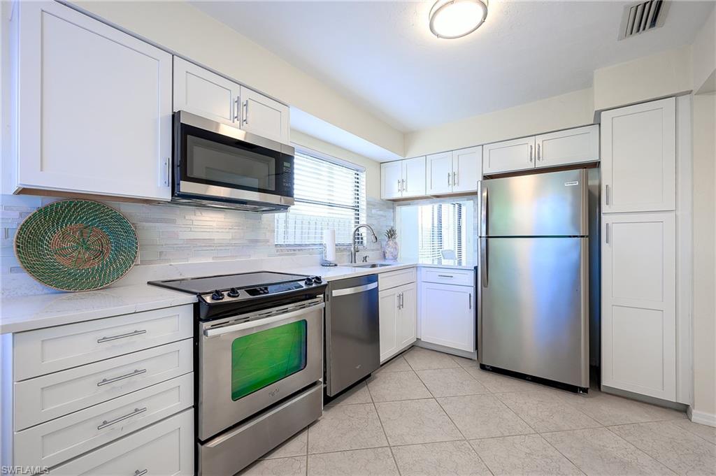 833 Reef Point Circle Naples, FL 34108 - Photo 5 of 41 Kitchen featuring appliances with stainless steel finishes, white cabinets, backsplash, and light stone counters