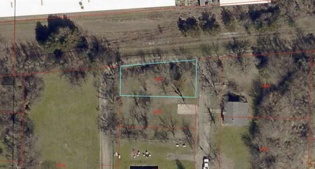 0 Norris Street Commerce, TX 75428 - Photo 2 of 2 This aerial image shows a rectangular plot of land surrounded by trees, located near a residential area. The plot appears to be clear and is outlined in blue, indicating its boundaries. There are nearby houses and open green spaces, suggesting a quiet, suburban setting.
