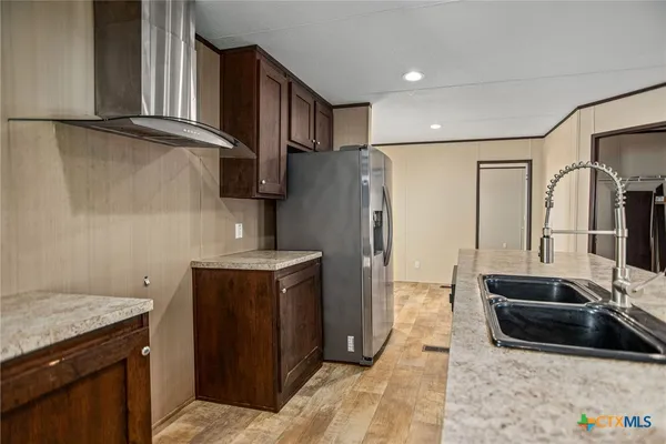 a kitchen with stainless steel appliances granite countertop a refrigerator a stove and a sink with wooden floors