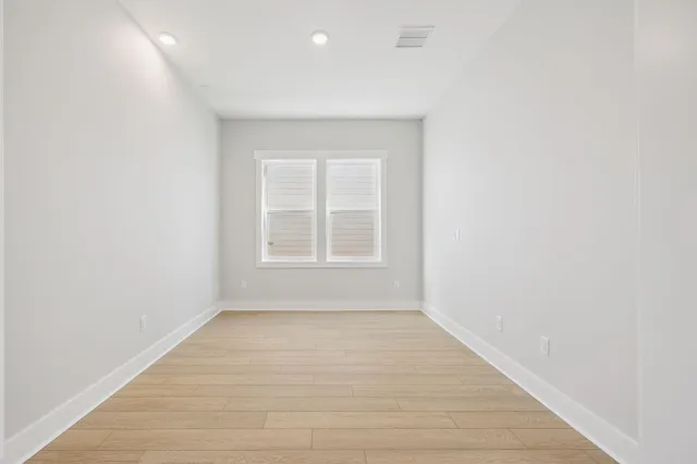 a view of an empty room with wooden floor and windows