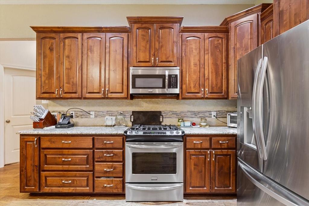 128 Creek Ridge Drive Waco, TX 76708 - Photo 15 of 40 Kitchen with appliances with stainless steel finishes, light wood-style flooring, brown cabinets, and tasteful backsplash