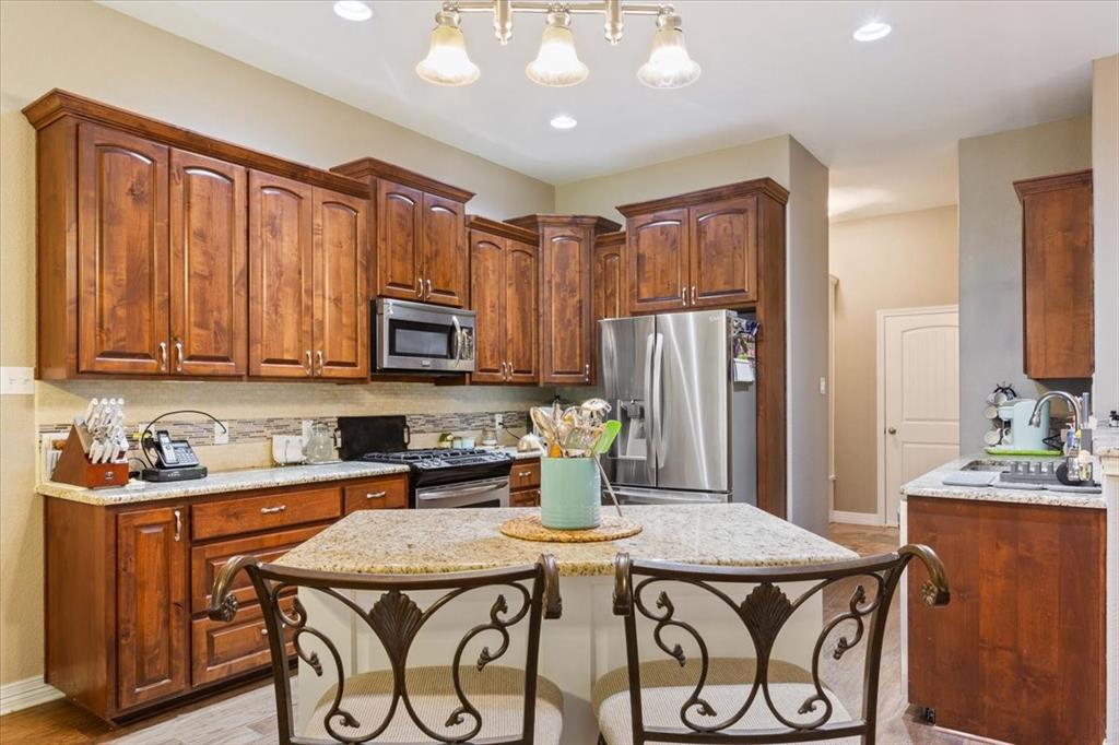 128 Creek Ridge Drive Waco, TX 76708 - Photo 16 of 40 Kitchen with appliances with stainless steel finishes, a breakfast bar, backsplash, baseboards, and light stone countertops