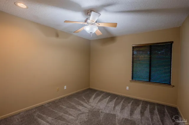 a view of an empty room with wooden floor and fan