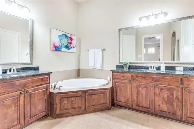 a spacious bathroom with a granite countertop double vanity sink a mirror and a bathtub