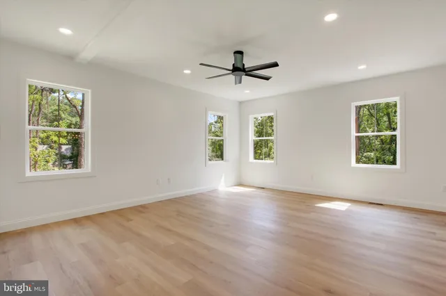 an empty room with wooden floor ceiling fan and windows