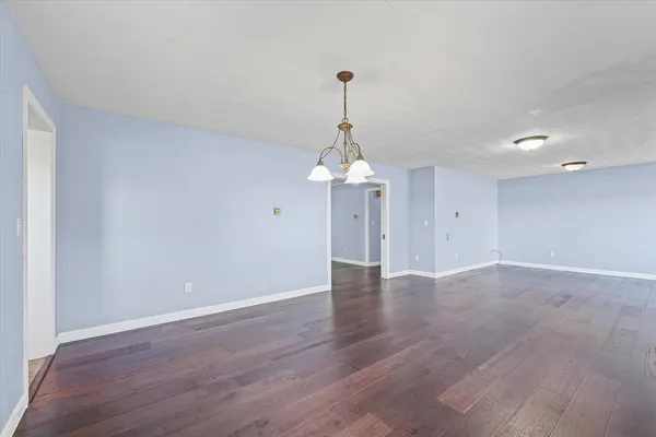 a view of an empty room with wooden floor fridge and a window