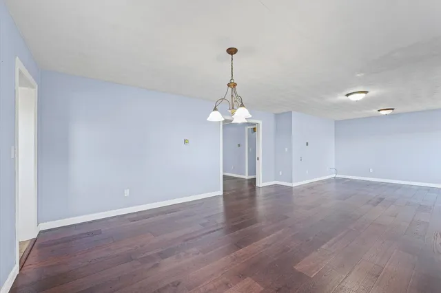 a view of an empty room with wooden floor fridge and a window