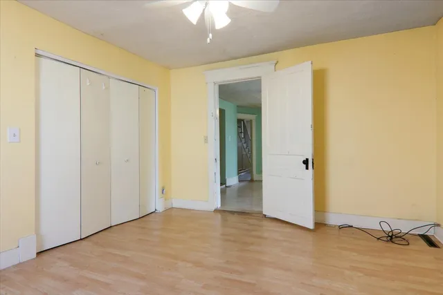 a view of an empty room with wooden floor and a ceiling fan