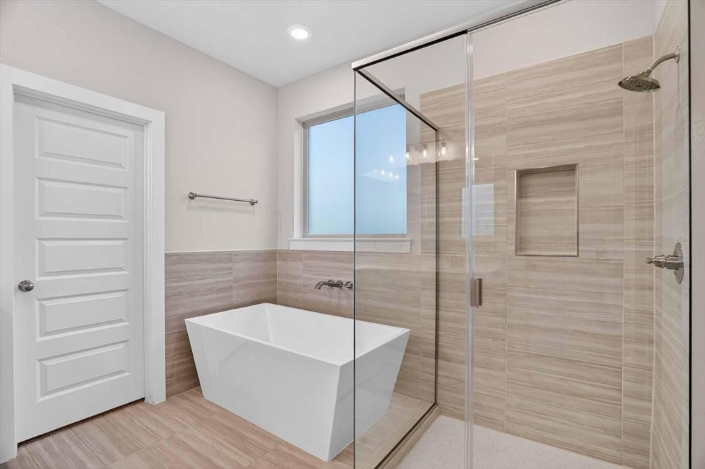 321 Skeen Peak Springtown, TX 76082 - Photo 37 of 37 Modern bathroom featuring a frameless glass shower enclosure, a freestanding soaking tub, large format tile flooring, and a tiled shower surround with a recessed niche