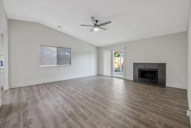 an empty room with wooden floor fireplace and windows