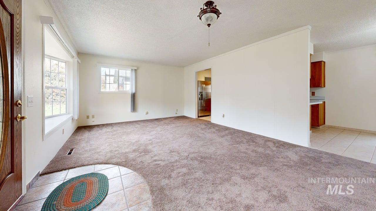196 Main Street Juliaetta, ID 83535 - Photo 6 of 27 Unfurnished living room with light colored carpet, light tile patterned flooring, and a textured ceiling