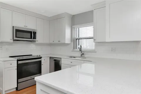 a kitchen with granite countertop white cabinets appliances a sink and a window