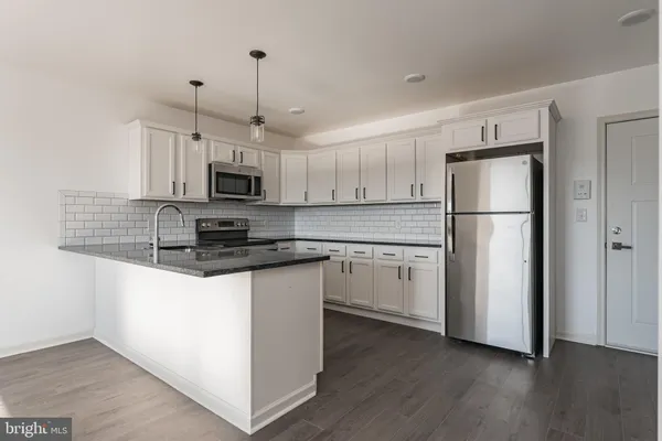 a kitchen with granite countertop a refrigerator a sink a stove a microwave and wooden floor