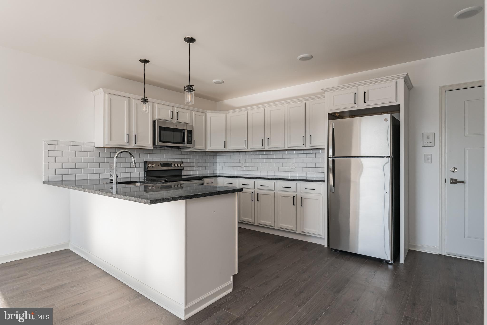 6649 Ridge Avenue, Unit A118 Philadelphia, PA 19128 - Photo 1 of 9 a kitchen with granite countertop a refrigerator a sink a stove a microwave and wooden floor
