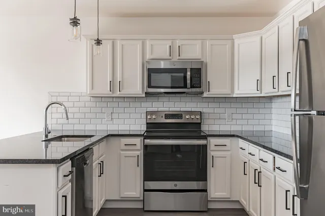 a kitchen with stainless steel appliances granite countertop white cabinets a sink a stove and a refrigerator
