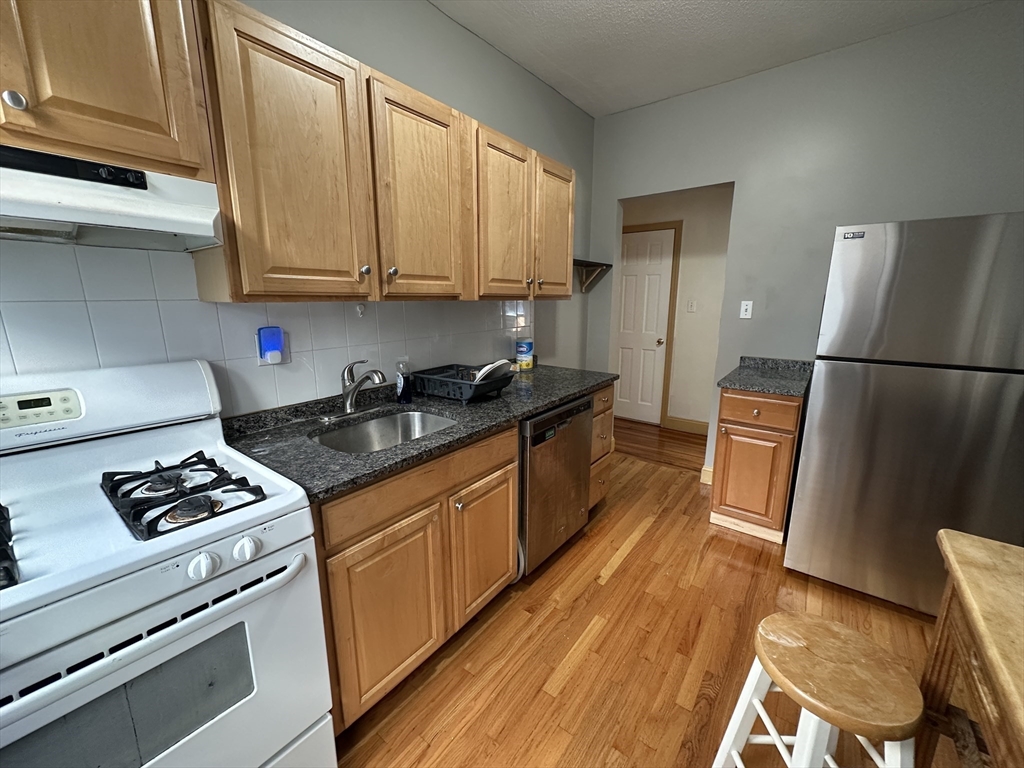181 Allston, Unit 2 Boston, MA 02134 - Photo 5 of 18 a kitchen with granite countertop stainless steel appliances a stove a refrigerator a sink and cabinets
