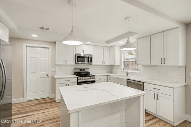 a kitchen with stainless steel appliances a stove a sink dishwasher a refrigerator white cabinets and wooden floor