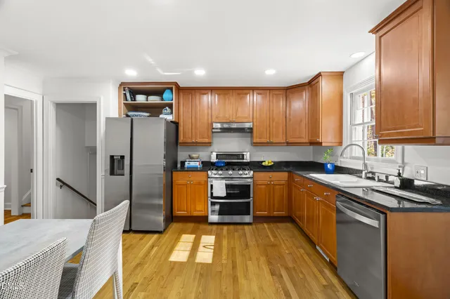 a kitchen with stainless steel appliances granite countertop a refrigerator a stove a sink a dining table and chairs with wooden floor