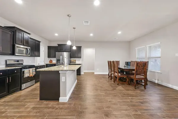 a kitchen with stainless steel appliances granite countertop a stove top oven a sink dishwasher a dining table and chairs with wooden floor