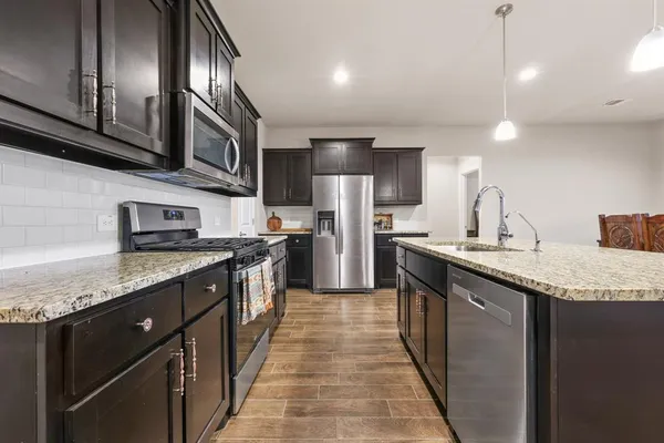 a kitchen with stainless steel appliances granite countertop a sink a stove top oven a refrigerator with wooden cabinets and floor